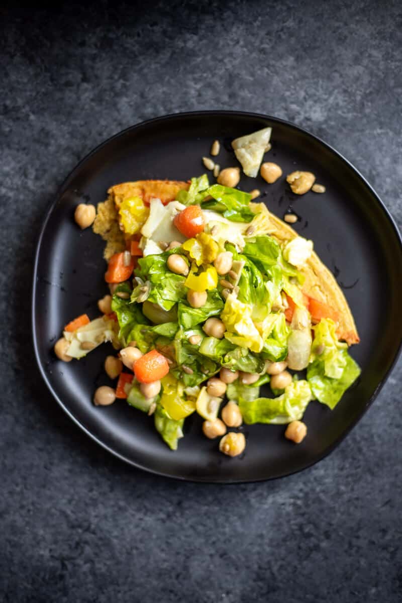 a triangle slice of socca salad pizza on a black plate